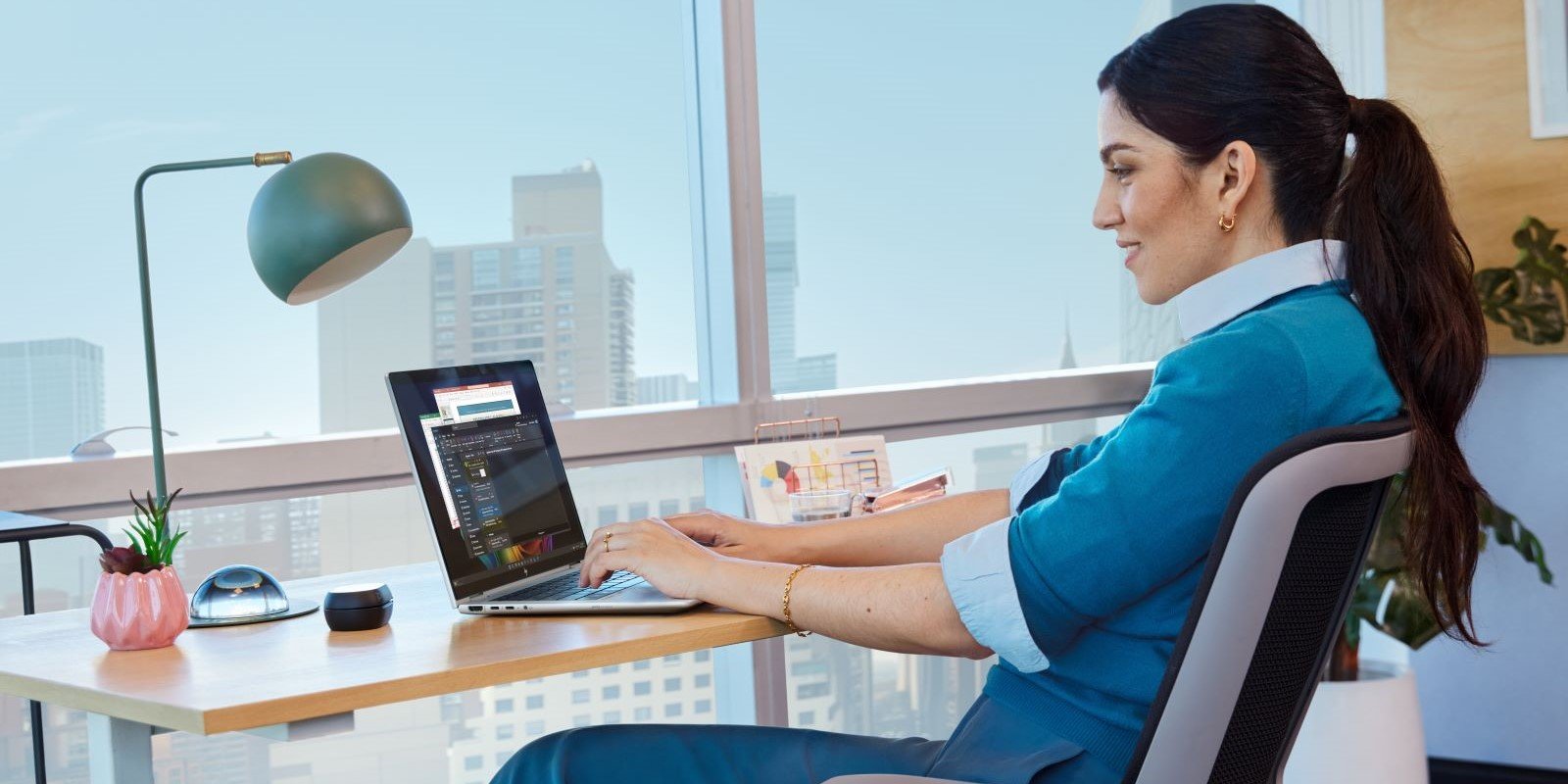 A woman in a blue blazer works with an HP EliteBook X AI PC laptop at a desk next to a window overlooking city buildings, with a modern desk lamp nearby.